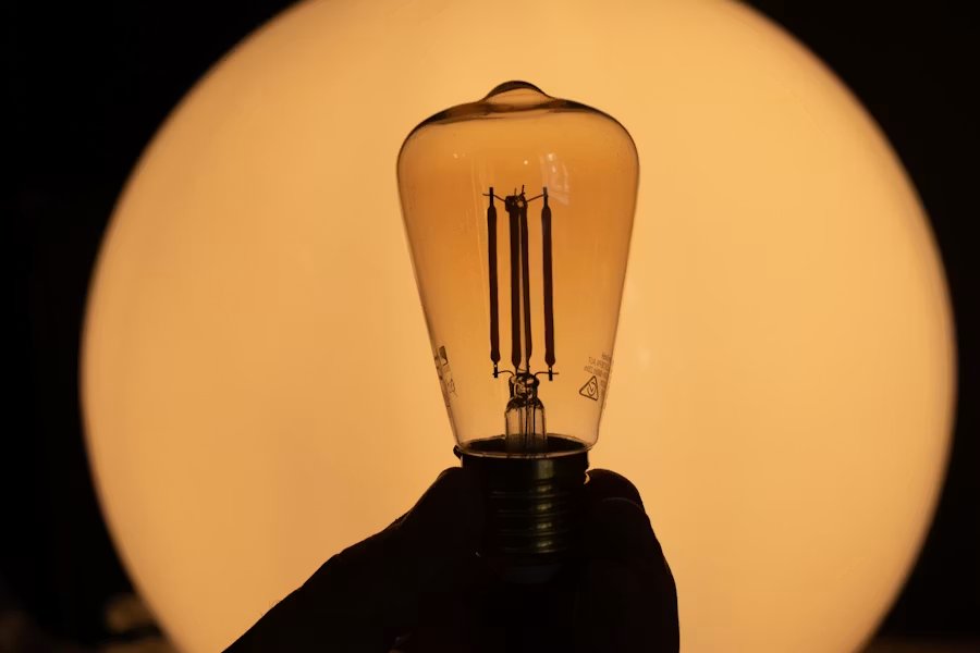A glowing filament lightbulb held against a warm light